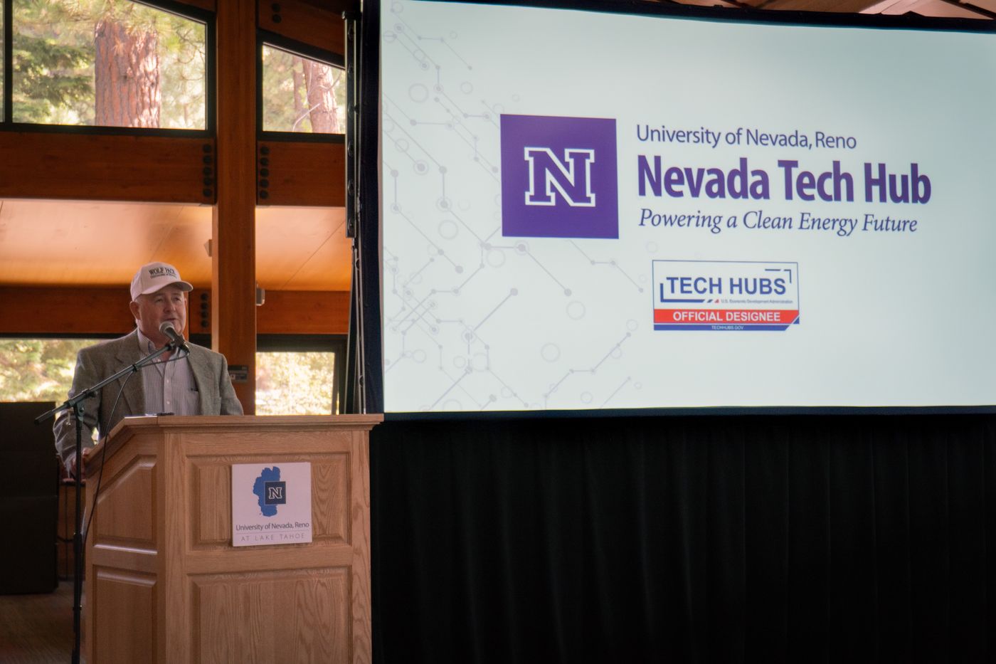 A speaker at the podium in front of a Nevada Tech Hub slide at the lab open house
